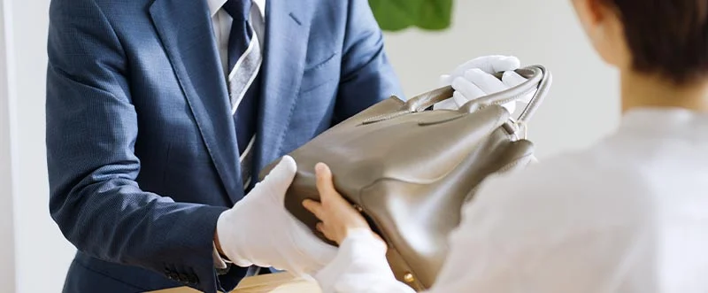 買取カウンターでバッグを両手で受け渡している様子